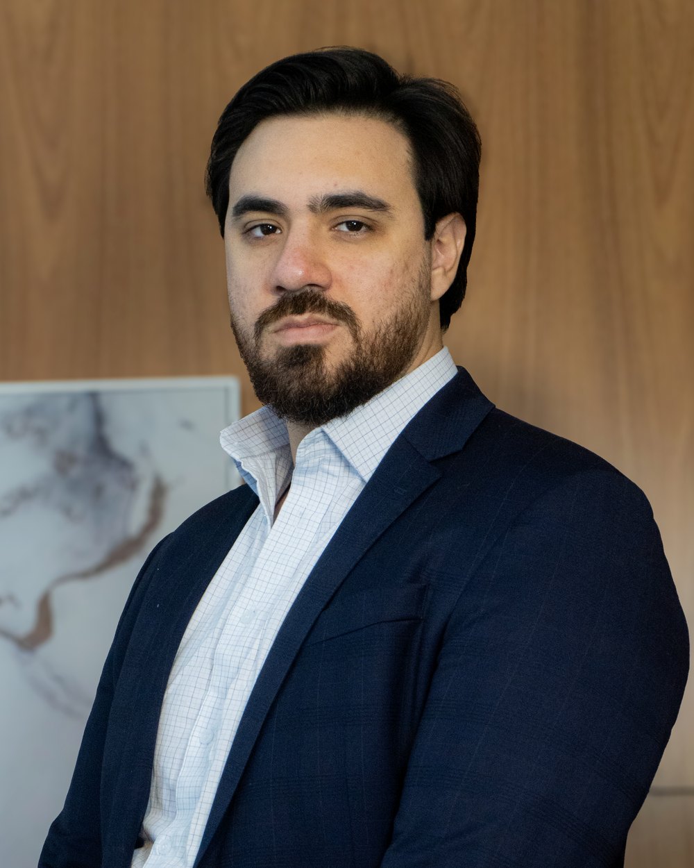 Bruno Oliveira, CEO e fundador do Grupo Brunello, de terno azul-marinho em frente a um painel de madeira.