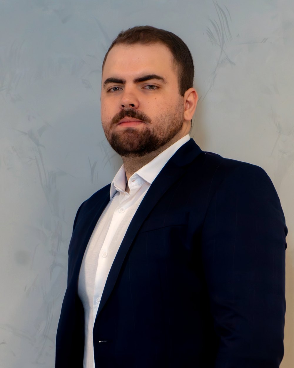 Vinicius Camilli, assessor de investimentos do Grupo Brunello, de terno azul-marinho em frente a uma parede clara.