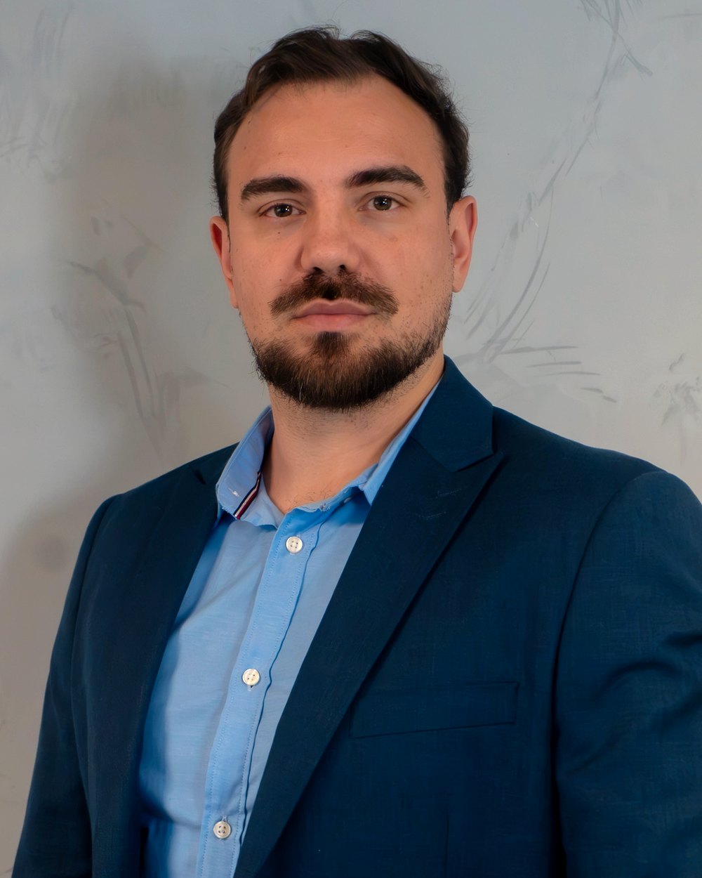 Vitor Diefenbach, head de produtos do Grupo Brunello, de terno azul em frente a uma parede clara.